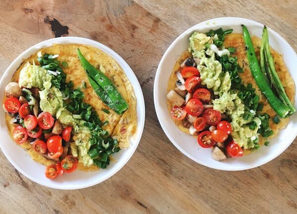 Two delicious omelette plates with avocado, tomatoes, and greens on a wooden table.